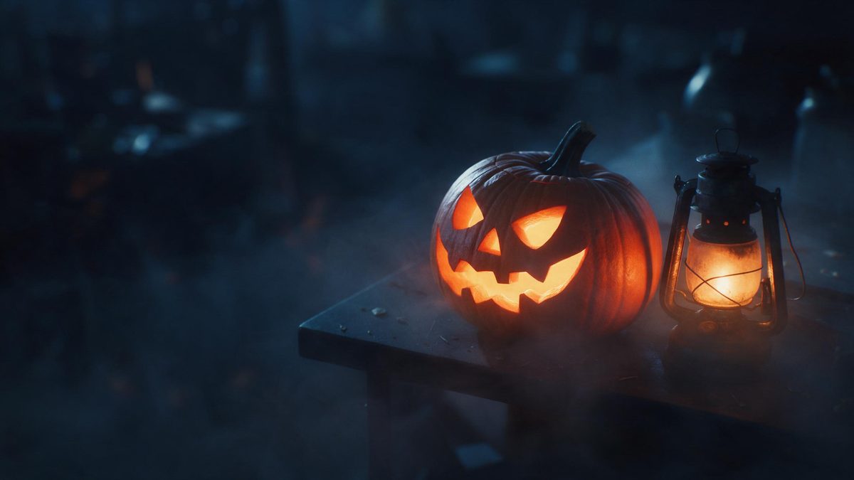 A dark worktable with a carved pumpkin and an old oil lantern, fog settling around them in warm light