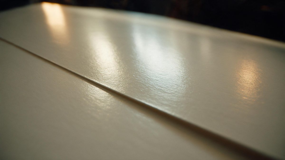 Extreme close-up of a glossy print surface at a raking angle, the texture and fibre of the paper visible, deep shadow beyond the edge