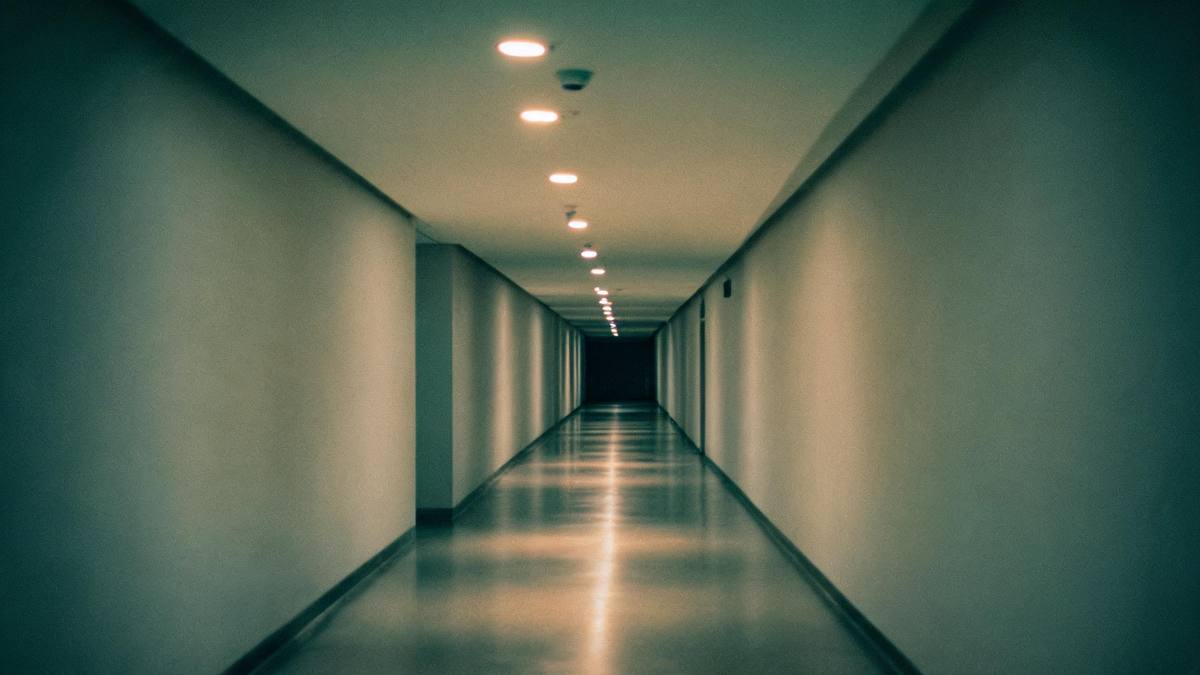 An empty long corridor in one-point perspective with ceiling lights receding into the distance