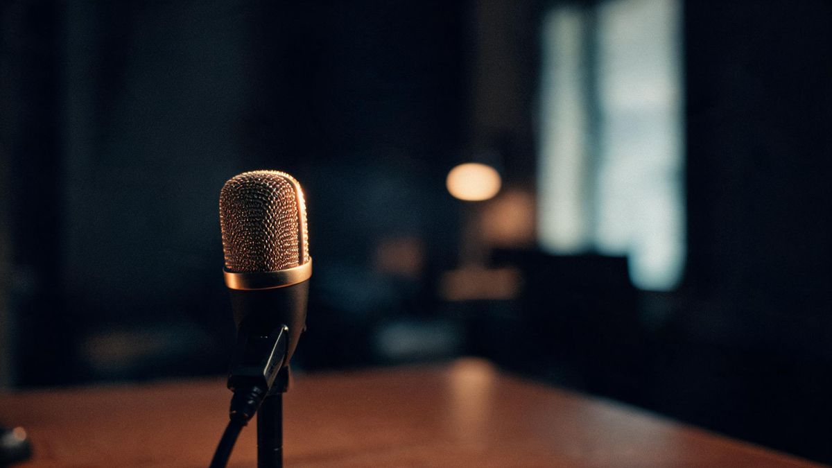 A microphone on a desk in a dim room with a warm rim light running along the grille
