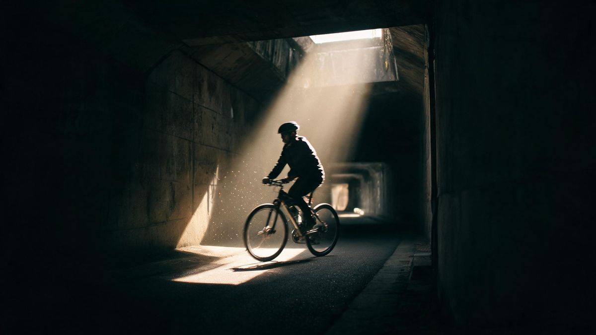 A cyclist passing through a shaft of light in a dark tunnel, the spokes blurred by motion
