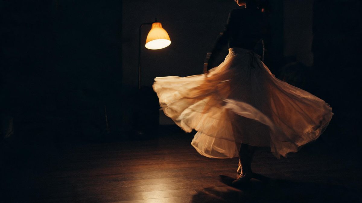 A dancer’s skirt caught mid-turn under a single warm lamp against a dark floor