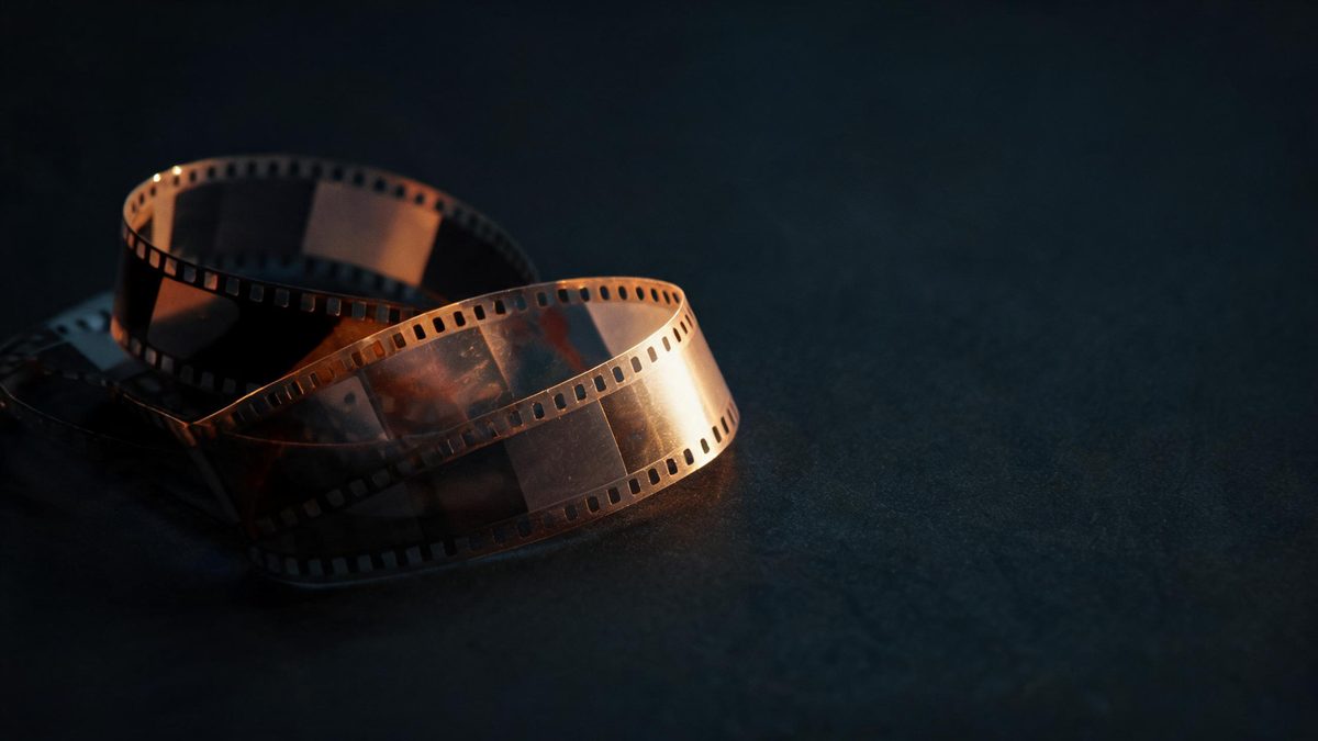 A strip of film negative coiled into two loose loops on a dark surface with one lit segment