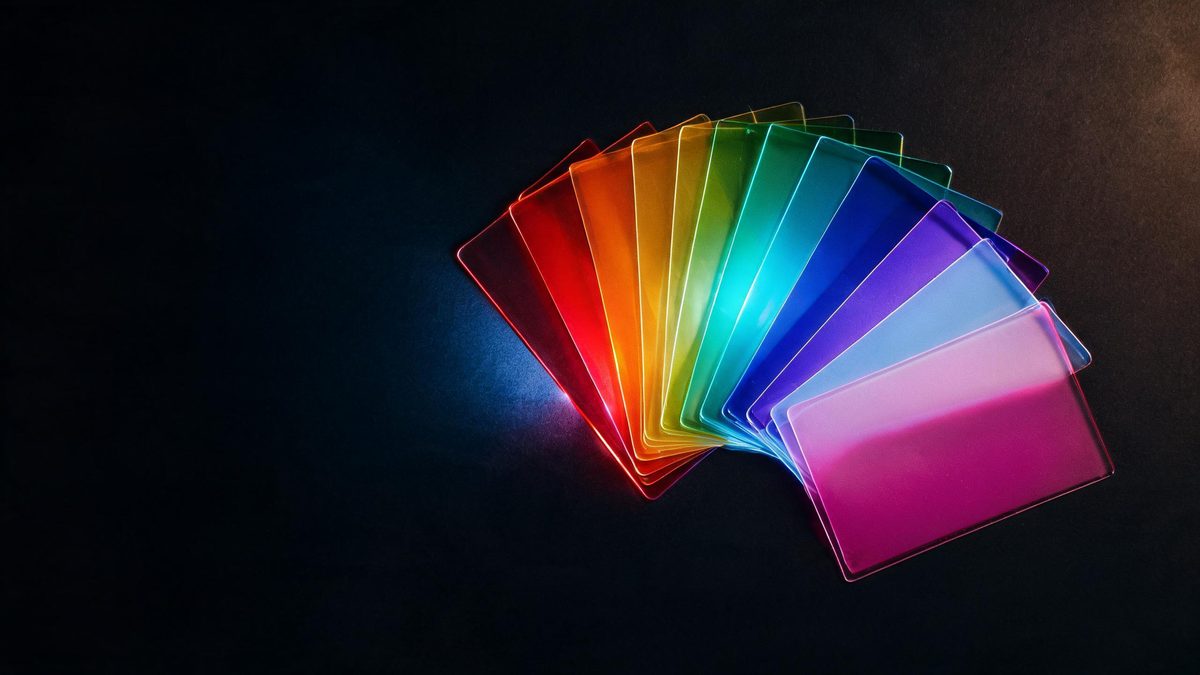 Ten translucent colour gel filters fanned out on black catching a cool rim light along one edge