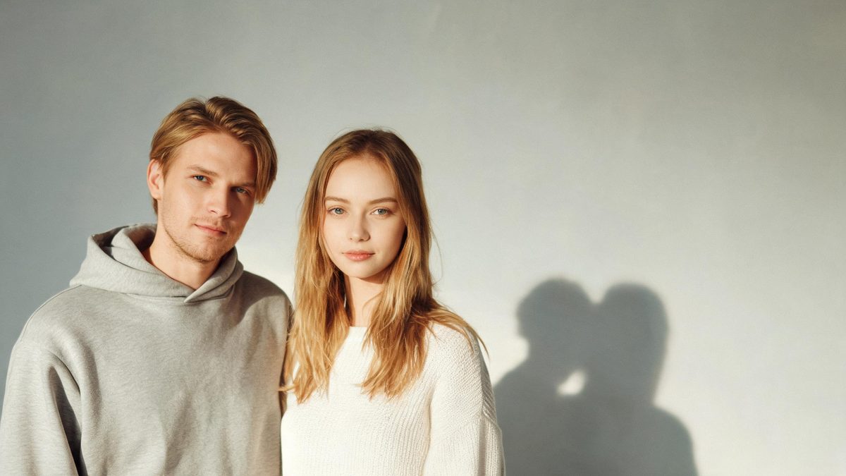 A two people in the same frame on a plain surface, lit from one side with soft shadow, broken apart at the moment of the cut