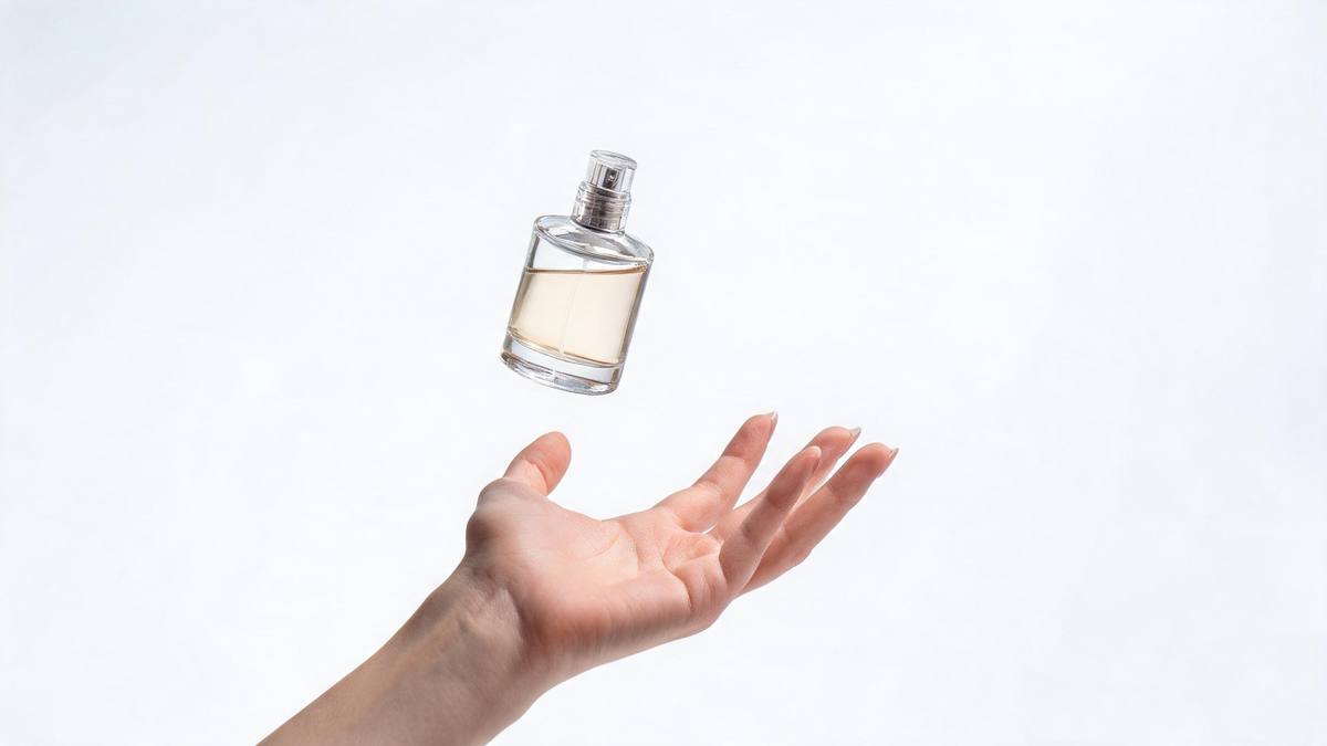 A hand catching a small glass perfume bottle mid-air against a plain studio background