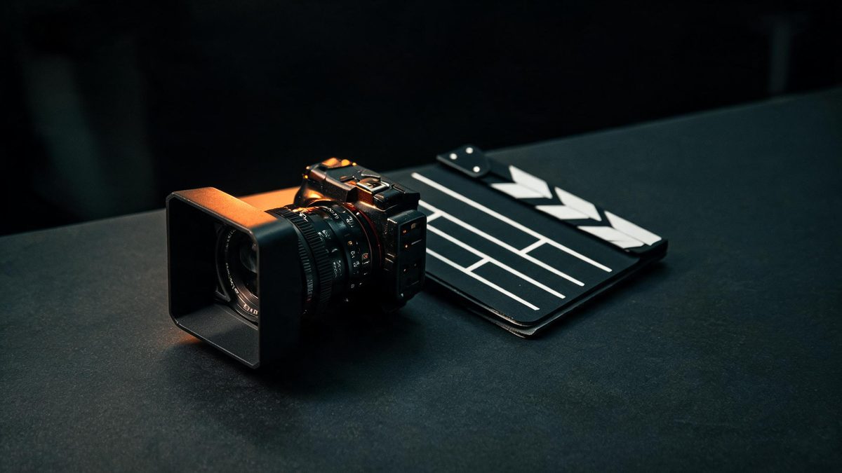 A cinema lens and matte box resting beside a folded director slate on a dark surface with one warm light bar