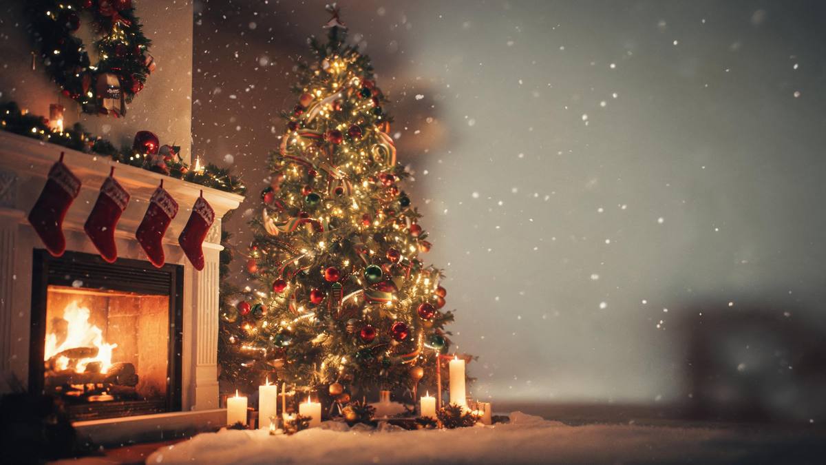A decorated Christmas tree beside a fireplace with stockings hanging from the mantel