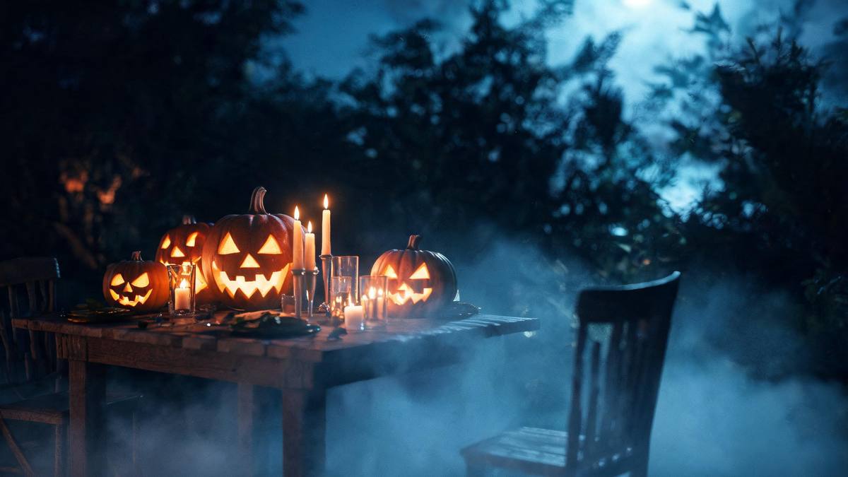 A Halloween table seen close with carved pumpkins and lit candles in warm low light