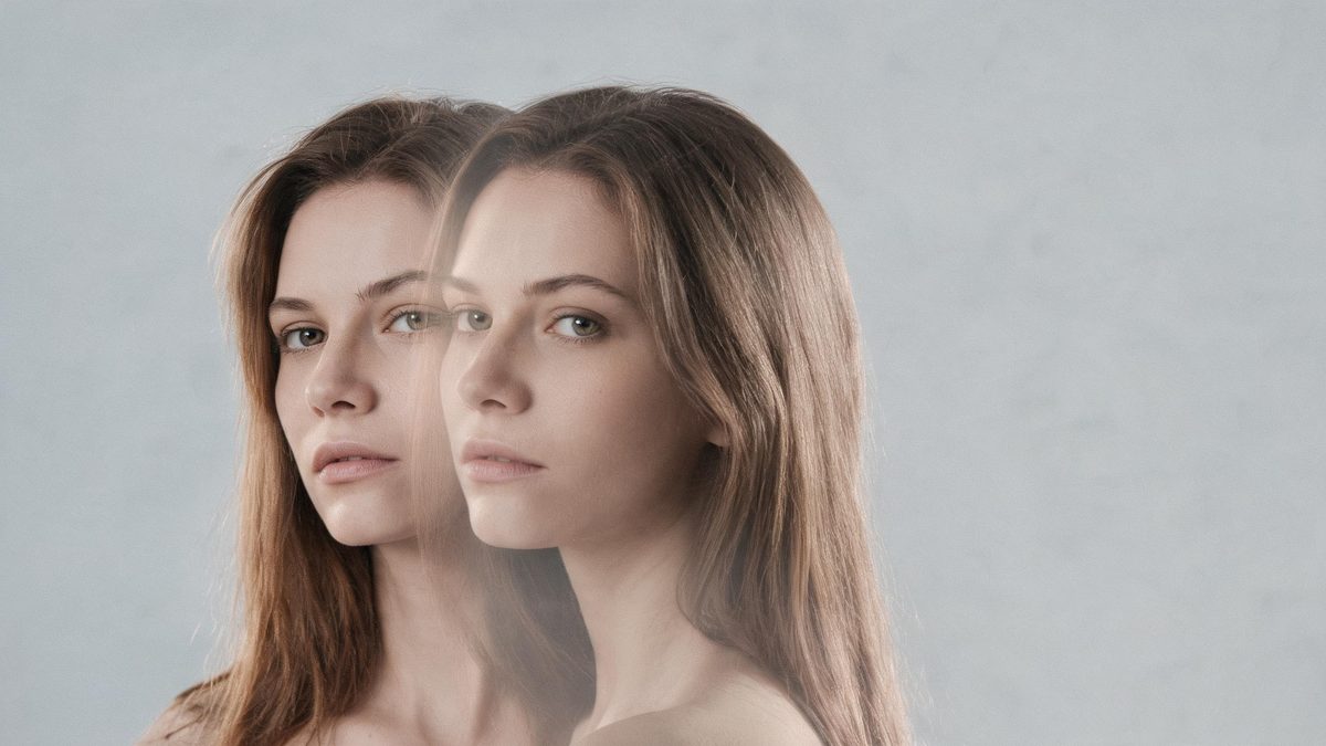 Two portraits of the same woman dissolving into one another in a soft blend on a neutral background