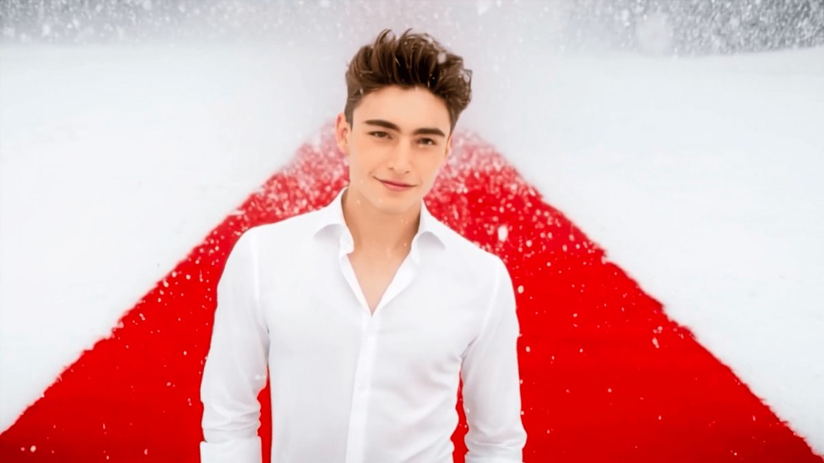 A person walking onto a red carpet in falling snow, lit for a nighttime gala entrance