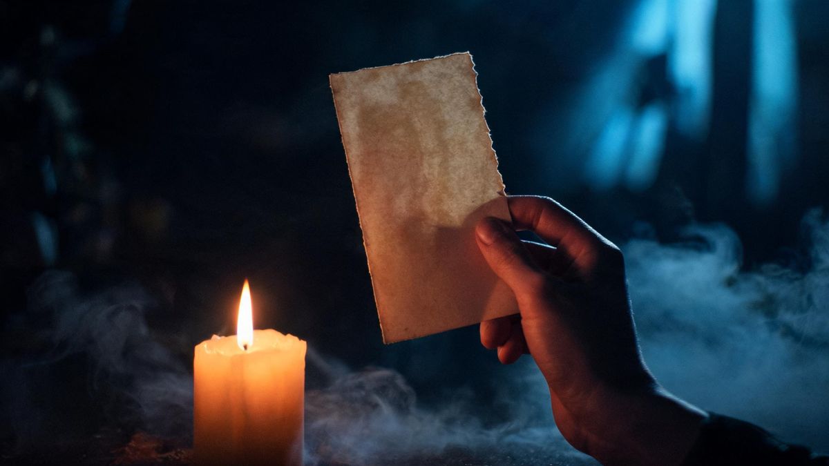 A hand holding an old photograph near a candle, the image turned away and unreadable