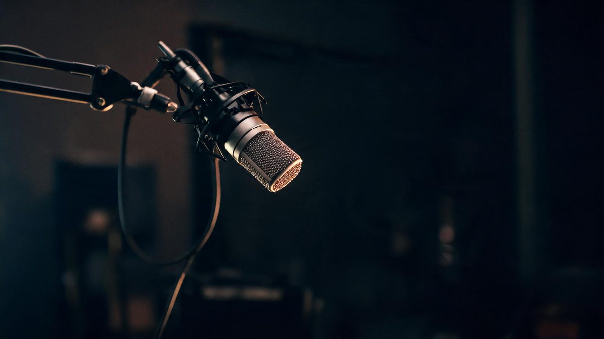 An empty studio microphone on a boom arm in a dark room with a warm rim light