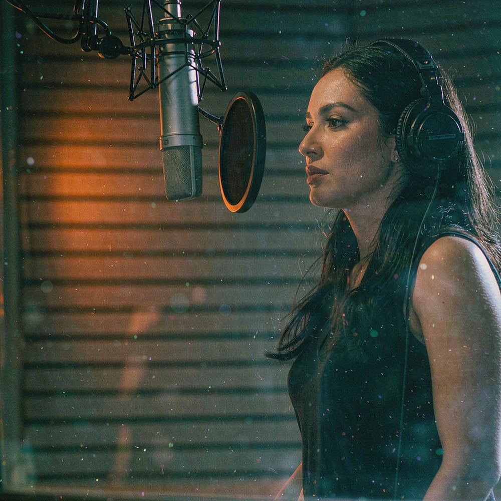 A voice actress recording behind studio glass at night, representing AI voiceover and dubbing by OpenFilmo